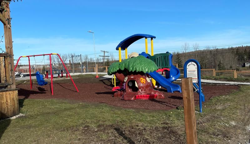 Image of a park with a play structure, swings, and benches. 