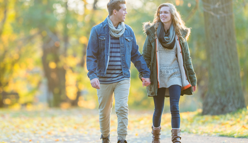 A stock image of a man and a woman holding hands and walking down a trail. 