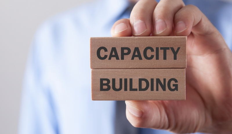 A photo of a man holding two blocks that read "capacity building". 